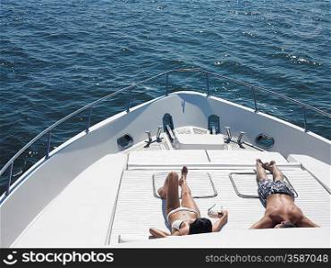 Young couple sunbathing on bow of yacht at sea elevated view