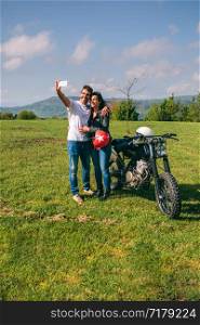 Young couple taking a selfie with a motorcycle outdoors. Couple taking a selfie with a motorcycle