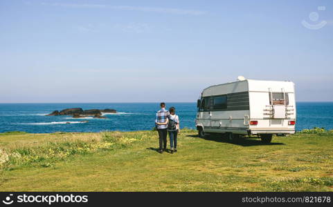 Young couple taking a walk near the coast with a camper in the background. Couple taking a walk near the coast with a camper