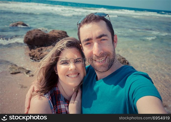 Young couple taking selfie with smartphone or camera at the beach.