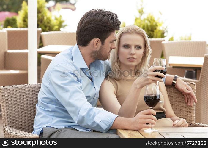 Young couple talking while having red wine at outdoor restaurant