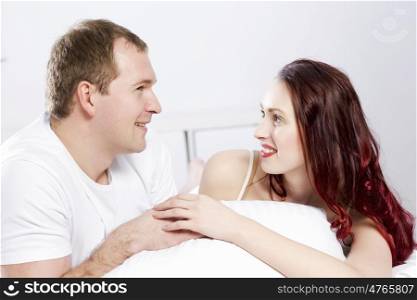 Young couple talking while lying in bed in the morning. Woke up together