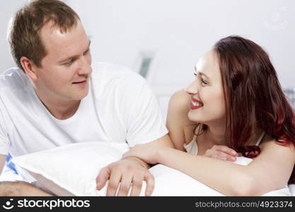 Young couple talking while lying in bed in the morning. Woke up together