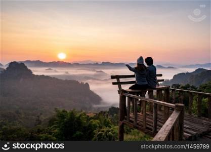 Young couple traveler looking at sea of mist and sunset over the mountain at Mae Hong Son, Thailand. Young couple traveler looking at sea of mist and sunset over the mountain