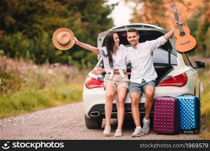 Young couple travelers sitting in trunk of a car on summer car vacation. Young couple tourist enjoying on summer vacation