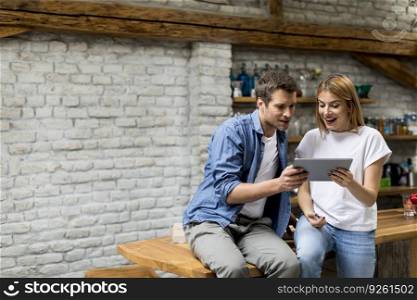 Young couple using a digital tablet and smiling while sitting on the table at rustic home
