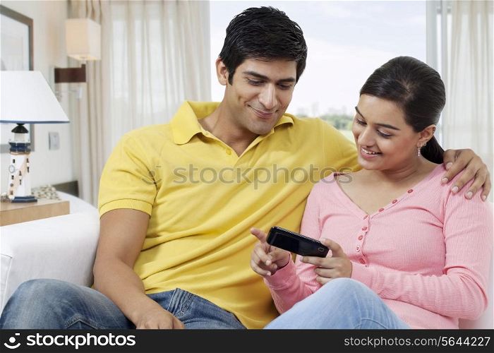Young couple using cell phone while sitting on sofa