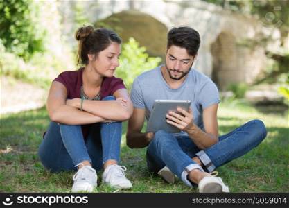 young couple using digital tablet at the park