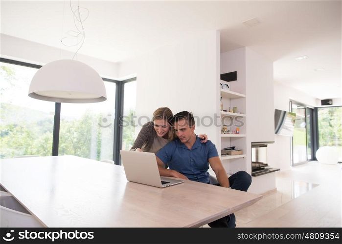 Young couple using laptop computer at luxury home together, looking at screen, smiling.
