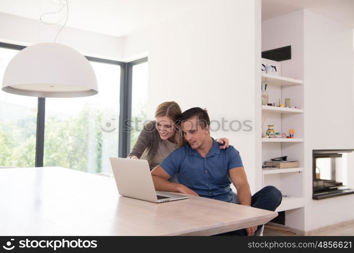 Young couple using laptop computer at luxury home together, looking at screen, smiling.