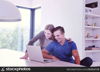 Young couple using laptop computer at luxury home together, looking at screen, smiling.