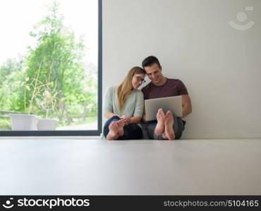 Young couple using laptop computer on the floor at luxury home together, looking at screen, smiling.