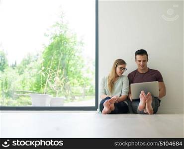 Young couple using laptop computer on the floor at luxury home together, looking at screen, smiling.