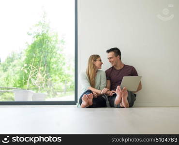 Young couple using laptop computer on the floor at luxury home together, looking at screen, smiling.