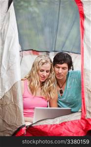 Young couple using laptop in tent while camping