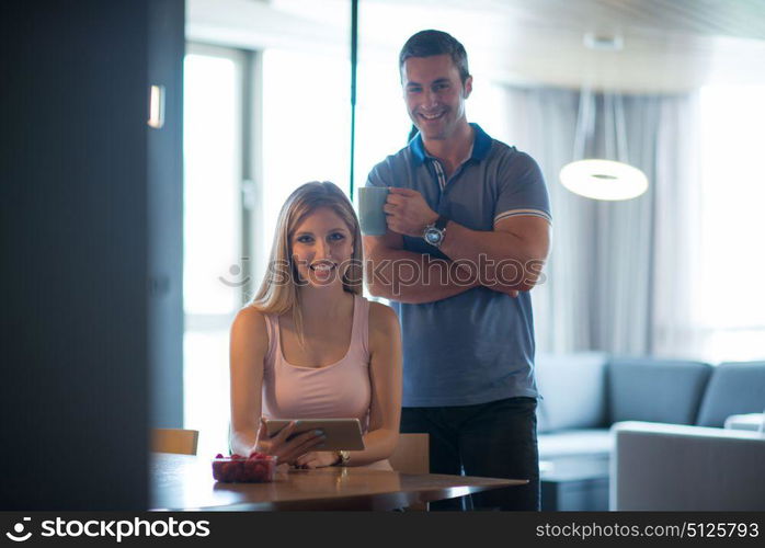 Young couple using tablet computer at luxury home together, looking at screen, smiling.