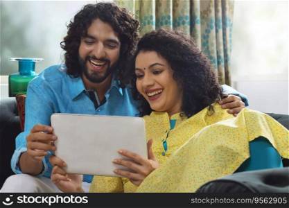 Young couple using tablet while sitting together on sofa at home