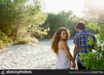 Young couple walking across sand, rear view