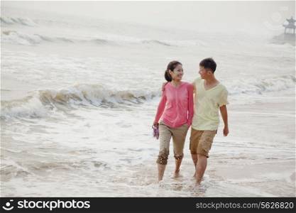 Young couple walking by the waters edge on the beach, China