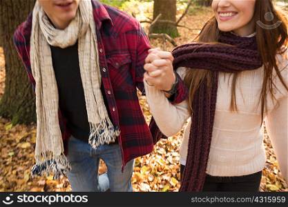 Young couple walking in forest, holding hands, mid section