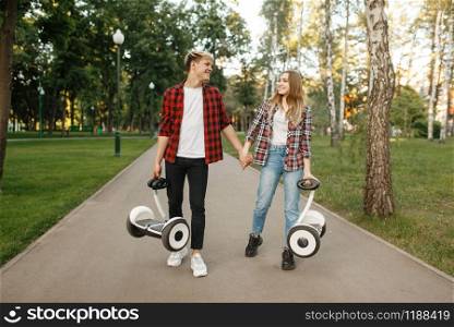 Young couple walking in summer park with gyro boards in hands. Outdoor recreation with electric gyroboard. Eco transport with balance technology, electrical gyroscope vehicle