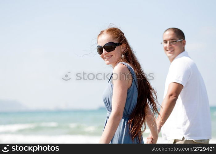 Young couple walking on the beach and posing the camera