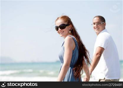 Young couple walking on the beach and posing the camera