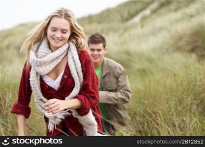 Young Couple Walking Through Sand Dunes Wearing Warm Clothing