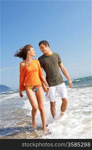 Young couple walking through surf on beach, front view