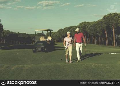 young couple walking to next hole on golf course. man carrying golf bag. couple walking on golf course