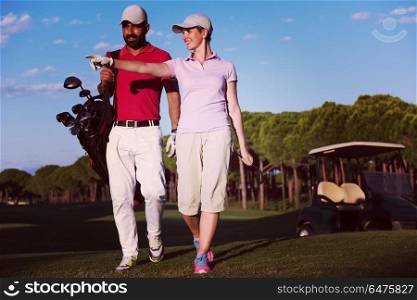 young couple walking to next hole on golf course. man carrying golf bag. couple walking on golf course