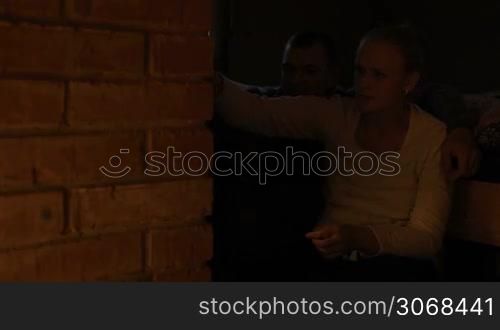 Young couple warming near stove in the evening. Woman opening the door and putting firewood into stove. Romantic atmosphere.