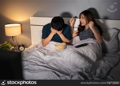 young couple watching sport tv on a bed with different emotions of win and lose