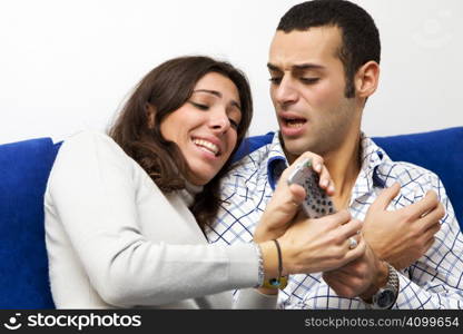 young couple watching tv and fighting to get the remote control