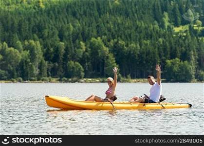 Young couple waving and rowing kayak on river summer vacation