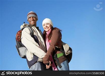 Young couple wearing backpacks standing outdoors holding hands.
