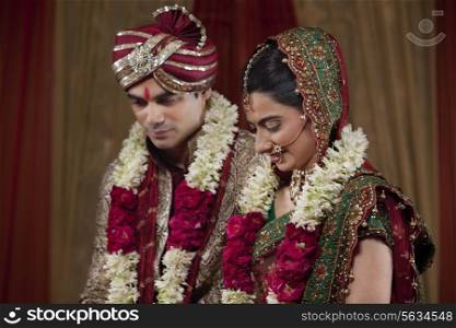 Young couple wearing garlands looking down
