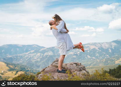 Young couple wearing white on the top of the mountain rock man holding his girl friend wife fiancee up hugging and kissing couple in love