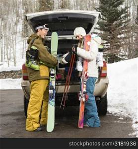Young couple wearing winter clothes unloading ski equipment from vehicle smiling and laughing.
