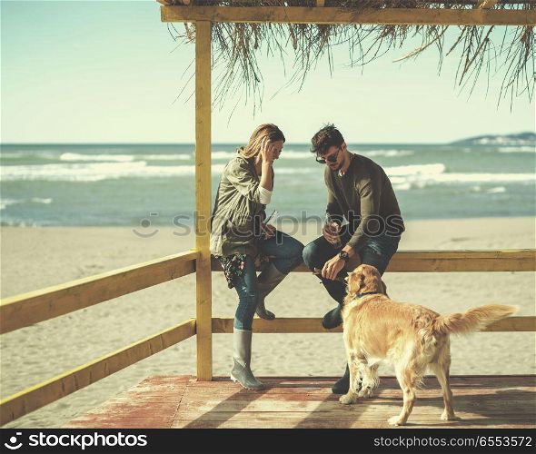 young couple with a dog at the beach. Couple with a dog Drinking Beer Together in empty beach bar during autumn time colored filter