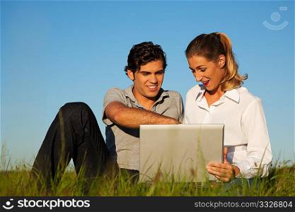 Young couple with a laptop computer surfing the internet outdoors on a meadow in beautiful yellow evening light