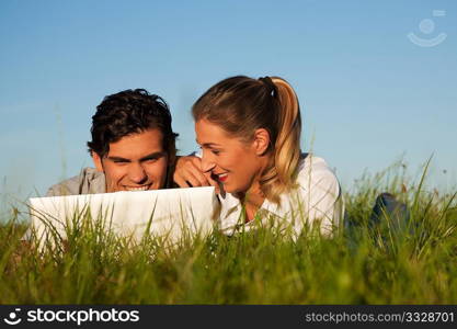 Young couple with a laptop computer surfing the internet outdoors on a meadow in beautiful yellow evening light