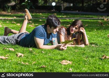Young couple with autumn leaf lying in park