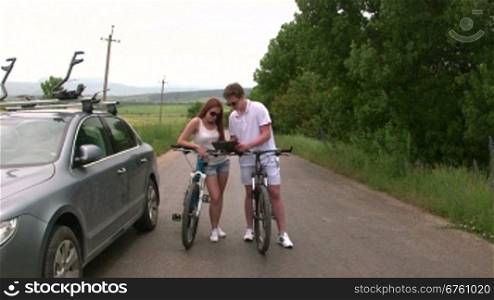 Young couple with bicycles near his car looking at map on tablet computer