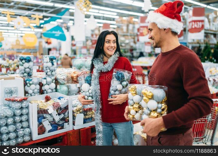 Young couple with boxes full of Christmas balls in shop, family tradition. December shopping of holiday goods and decorations. Young couple with boxes full of Christmas balls