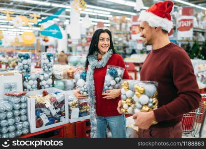 Young couple with boxes full of Christmas balls in shop, family tradition. December shopping of holiday goods and decorations. Young couple with boxes full of Christmas balls