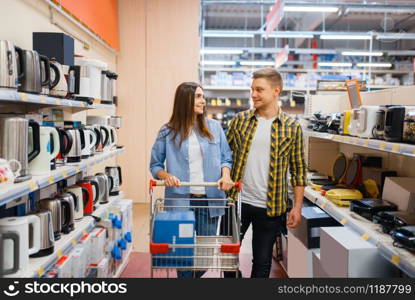 Young couple with cart in electronics store. Man and woman buying home electrical appliances in market. Young couple with cart in electronics store