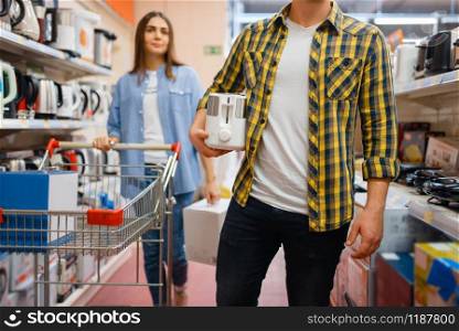 Young couple with cart in electronics store. Man and woman buying home electrical appliances in market. Young couple with cart in electronics store