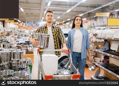 Young couple with cart in houseware store. Man and woman buying home goods in market, family in kitchenware supply shop. Young couple with cart in houseware store