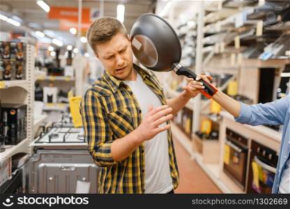 Young couple with frying pan in electronics store. Man and woman buying home electrical appliances in market. Young couple with frying pan in electronics store